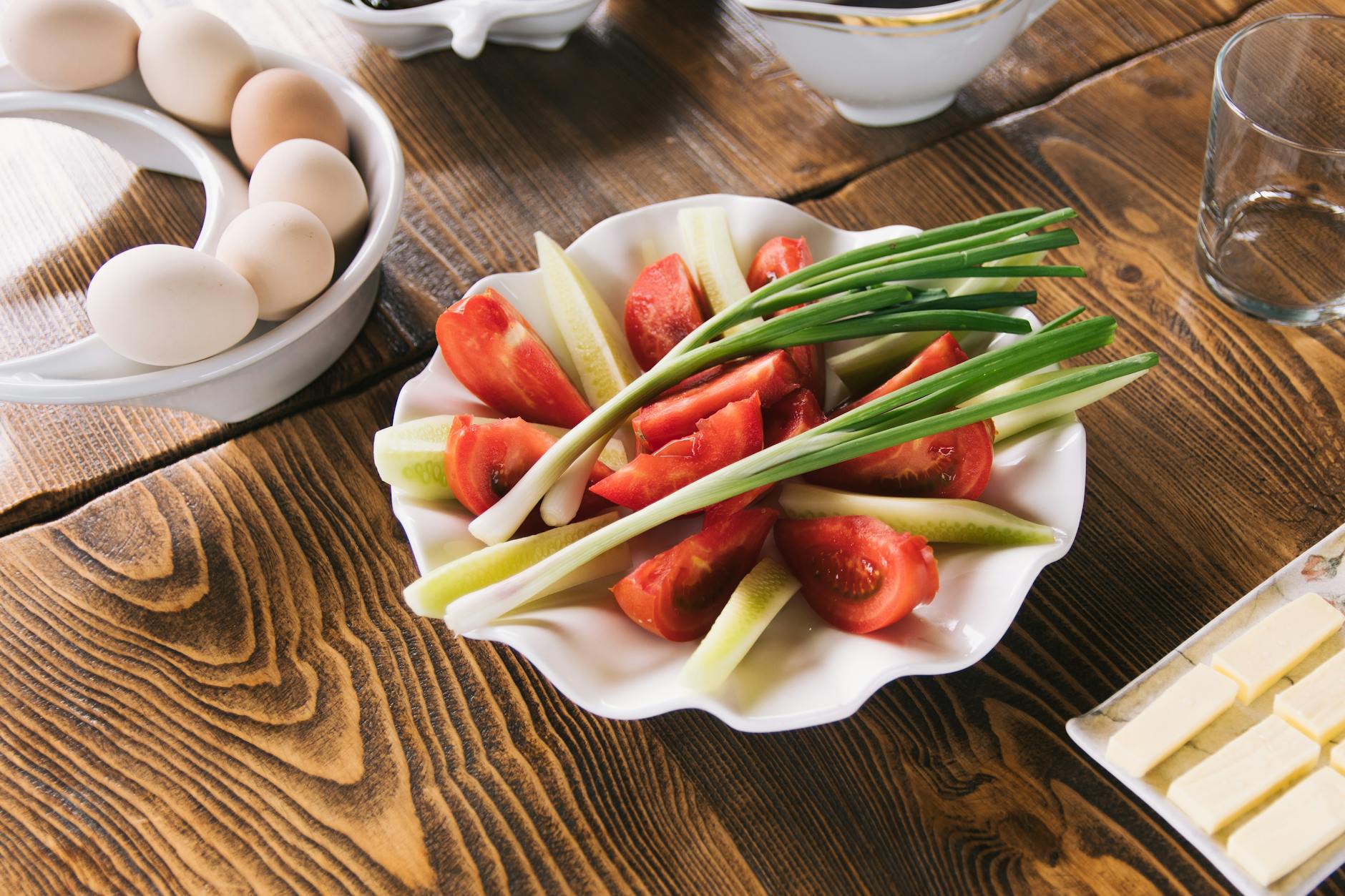 Talerz pomidorów, ogórków i szczypiorku obok jajek na drewnianym stole