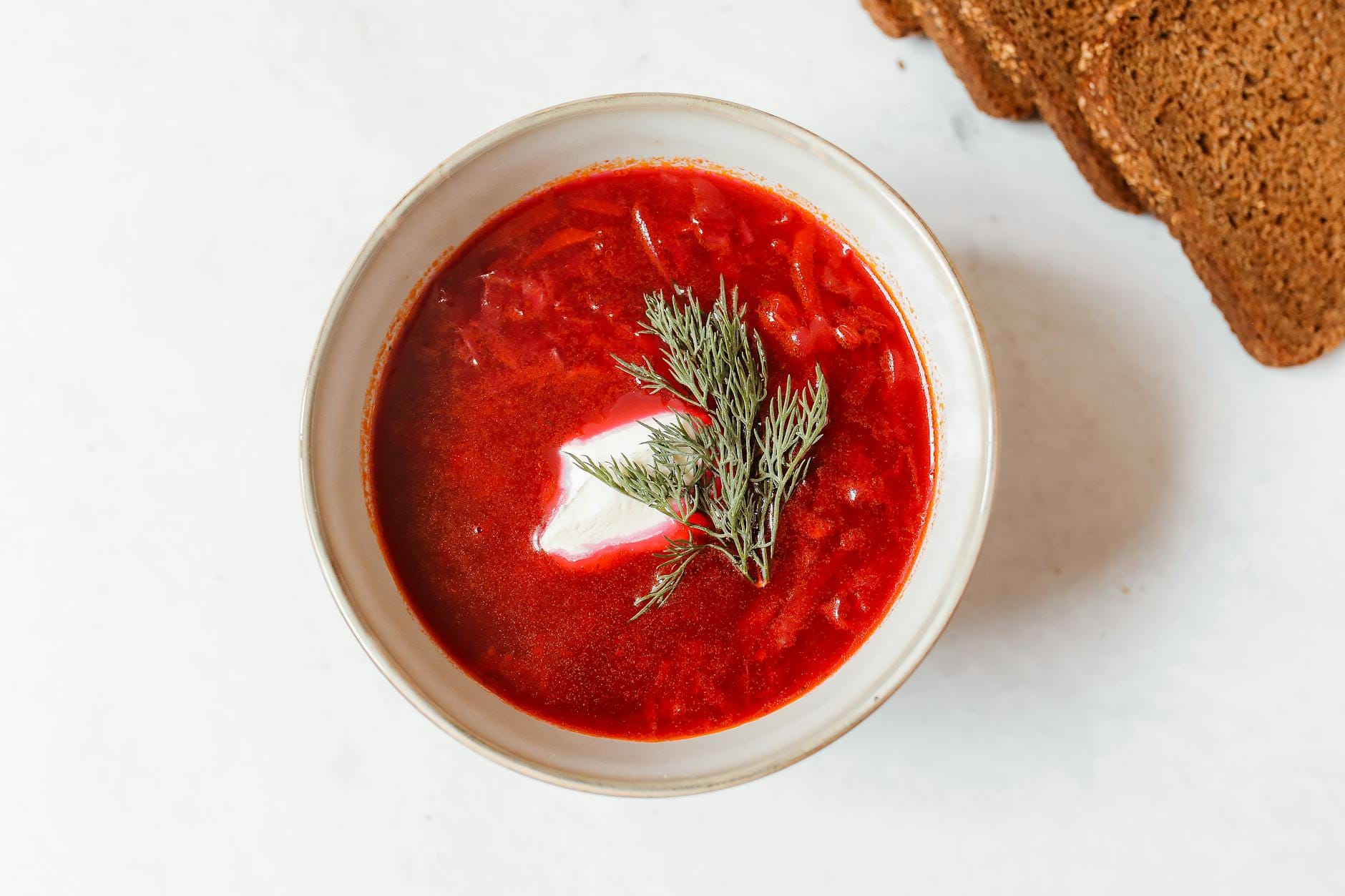 Barszcz czerwony z dodatkami w misce z góry, obok kromki chleba żytniego