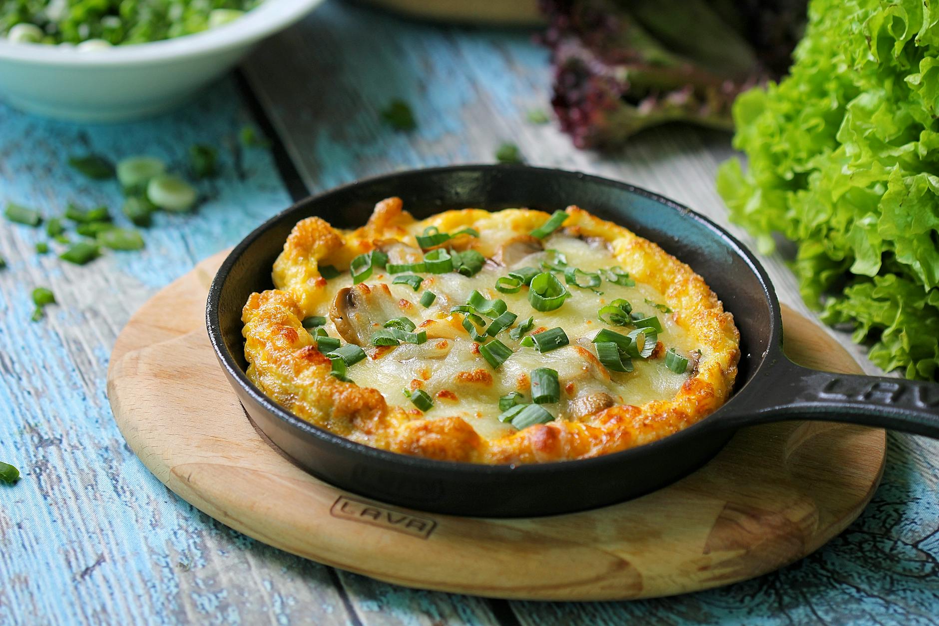 Omlet z serem i szczypiorkiem na patelni na drewnianej desce