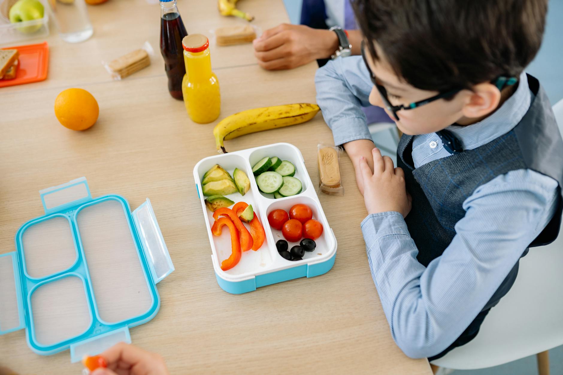 Chłopiec je zdrowy obiad z kolorowego lunchboxa przy szkolnym stoliku