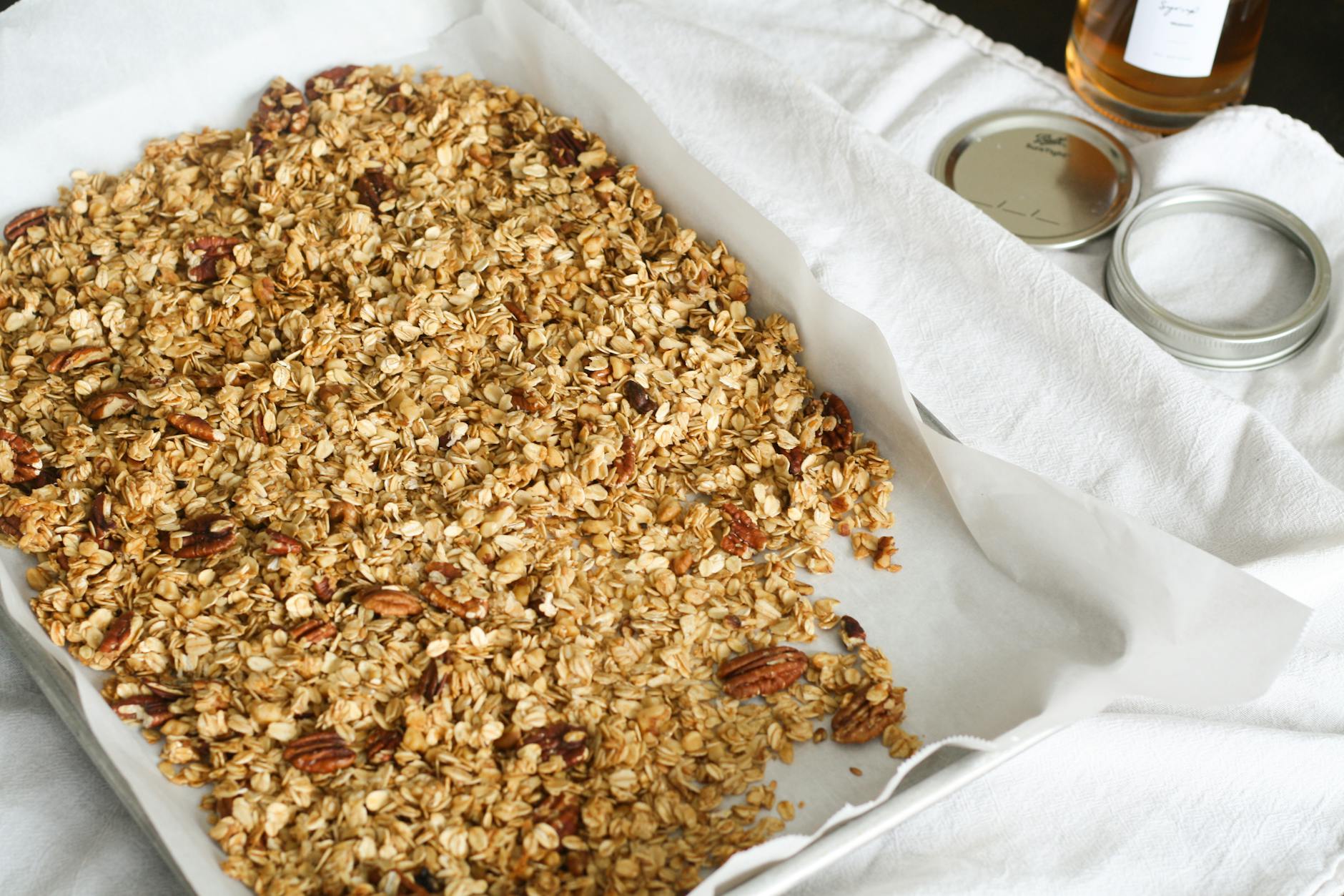 Domowa granola z płatków owsianych i orzechów na blasze obok słoika miodu Domowa granola z płatków owsianych i orzechów na blasze obok słoika miodu