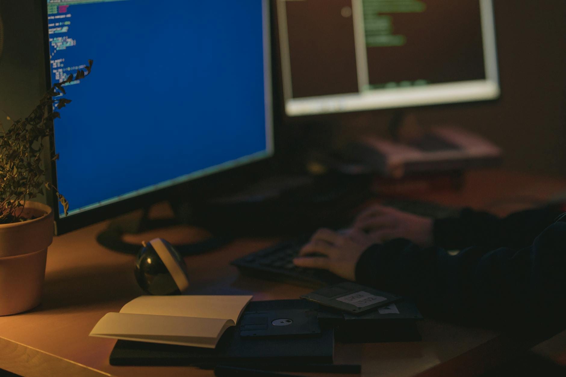 Programista pracuje przy dwóch monitorach w ciemnym pomieszczeniu