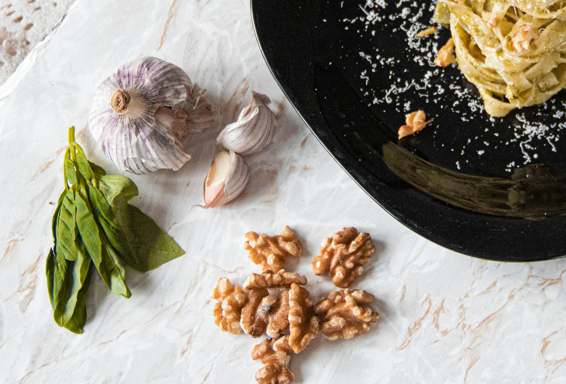 Makaron z pesto, świeża bazylia, czosnek i orzechy na blacie z marmuru