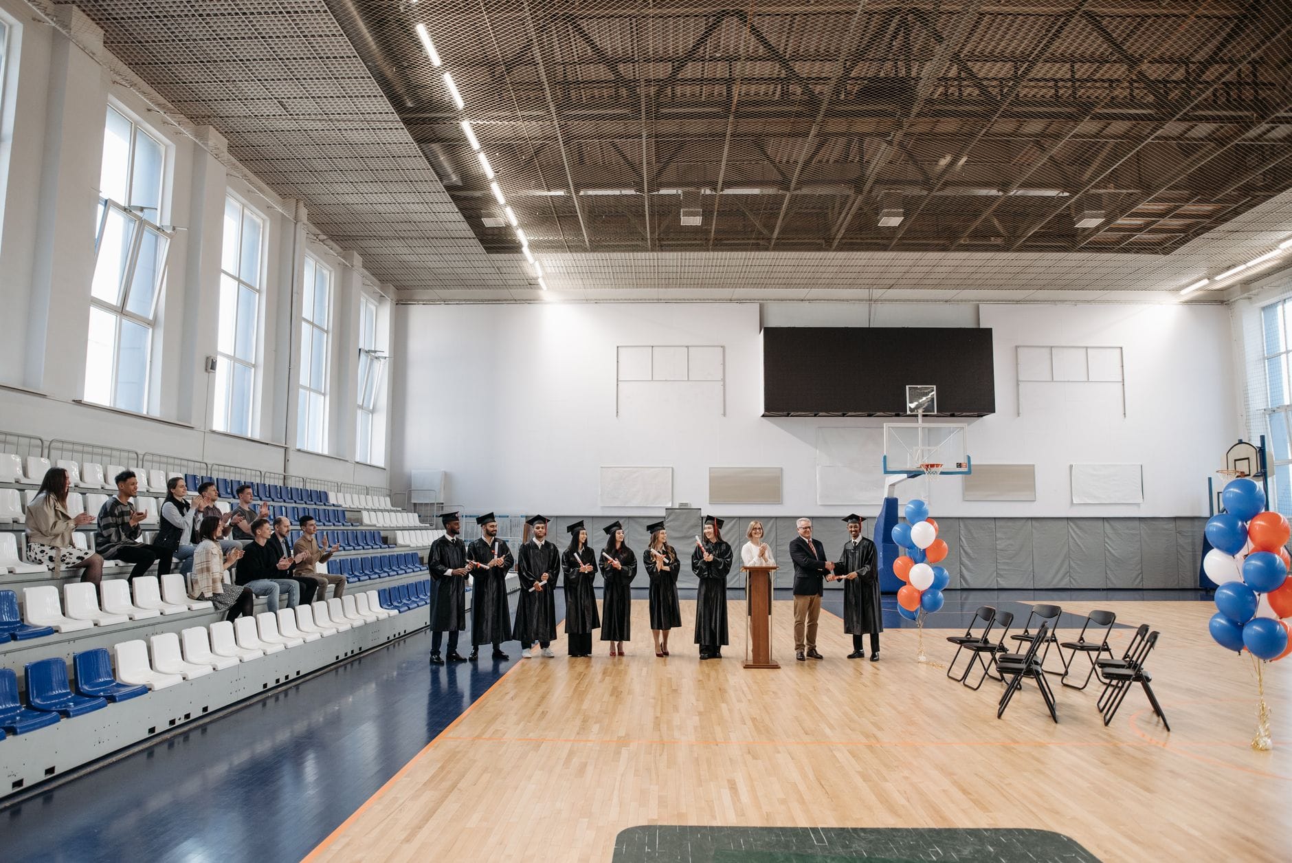 Absolwenci odbierają dyplomy w sali gimnastycznej pełnej publiczności Absolwenci odbierają dyplomy w sali gimnastycznej pełnej publiczności