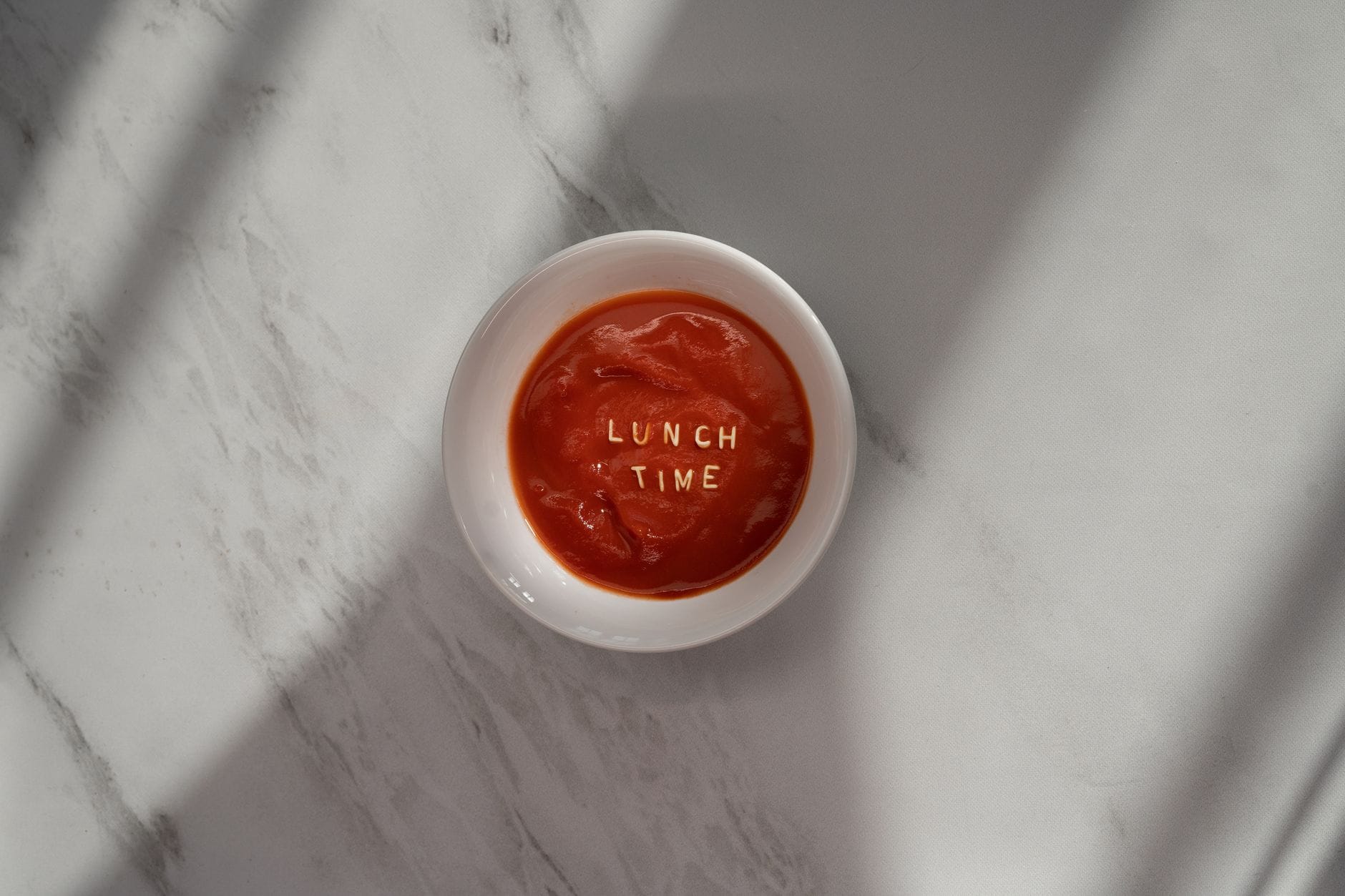 Miska zupy pomidorowej z napisem lunch time na jasnym blacie