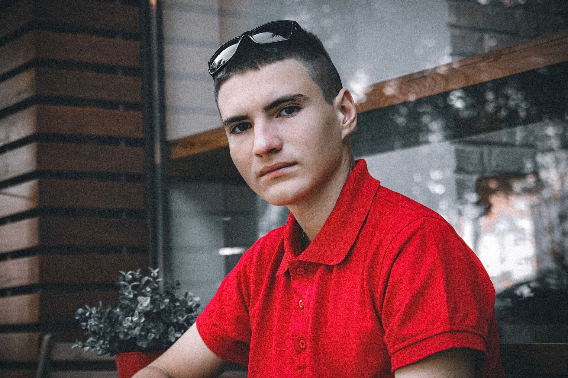 Młody mężczyzna w czerwonej koszulce polo patrzy w kamerę w mieszkaniu